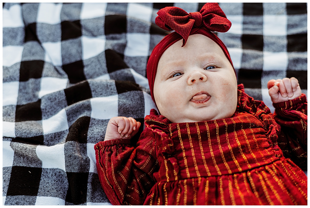 baby girl sticks out tongue in red outfit with bow by Ellie Chavez Photography