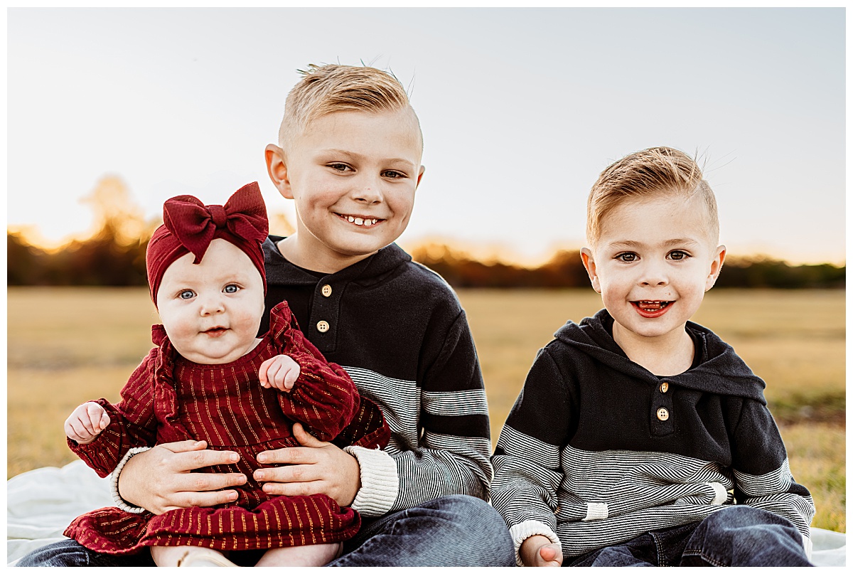 siblings grin as they sit together by Austin portrait photographer