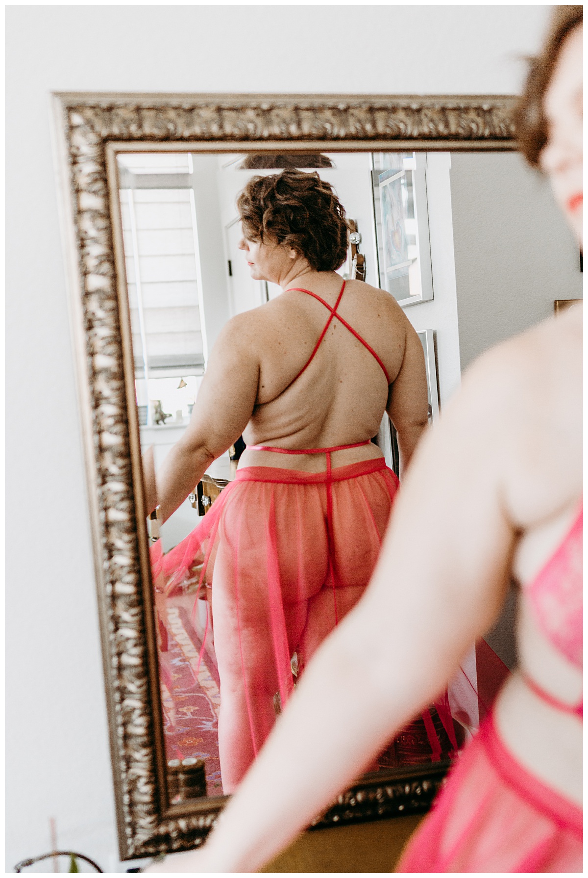 woman stands with back to mirror at pink boudoir session