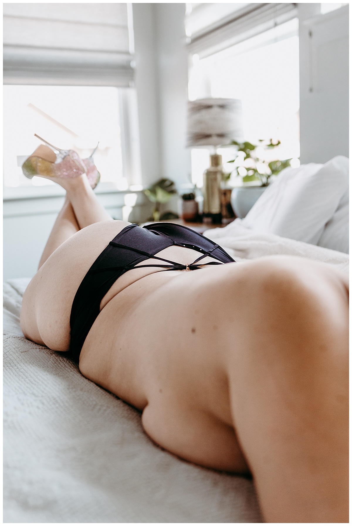 high heeled lady lays on stomach on bed in black panties by Ellie Chavez Photography